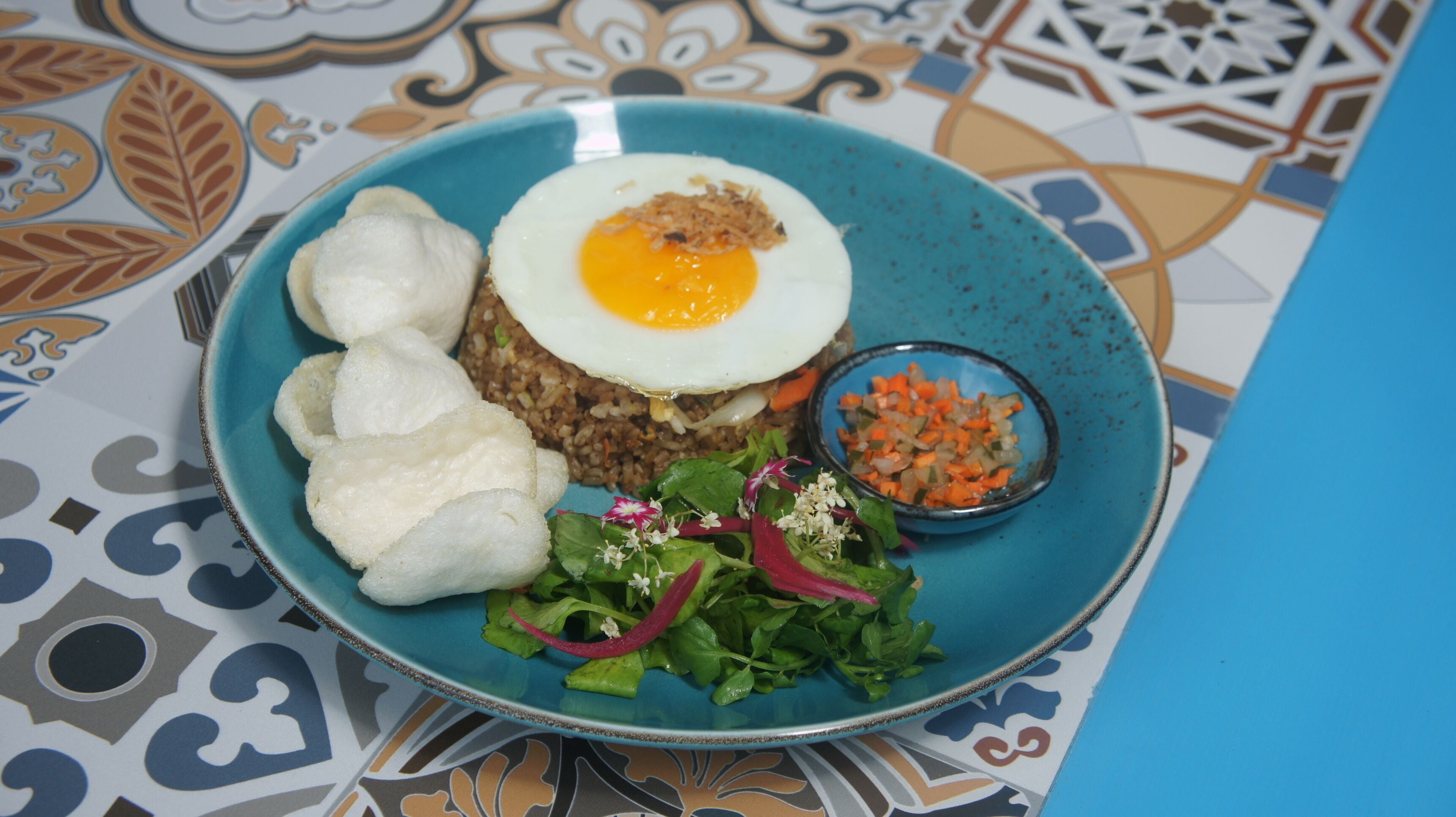 Un plato con arroz, un huevo frito, albóndigas, una ensalada y un tazón pequeño de verduras.