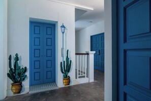 Un pasillo con puertas azules, barandilla blanca y cactus en macetas.