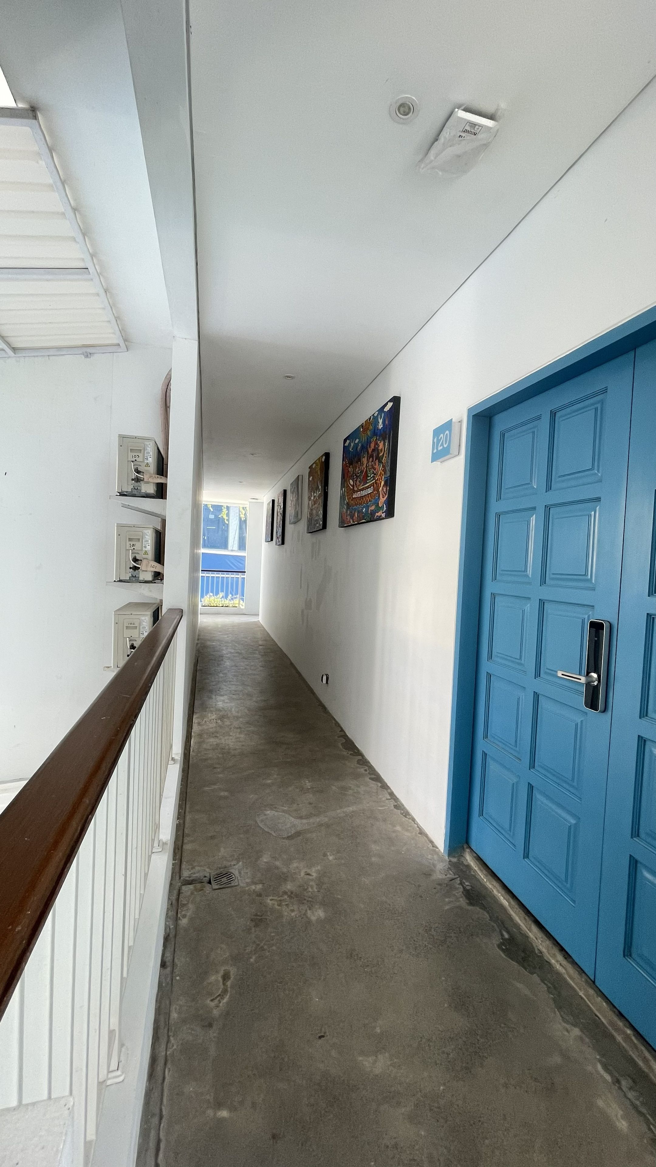 A corridor with a blue door, white walls, and a wooden handrail.