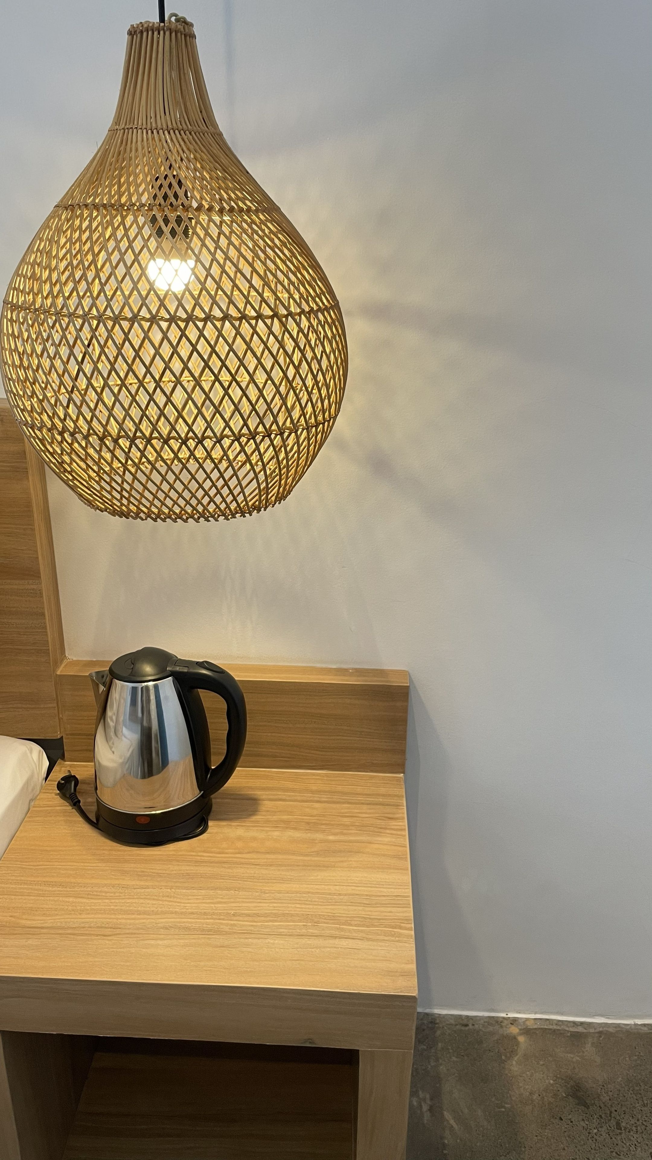 A bedside table with a kettle and a woven lamp.