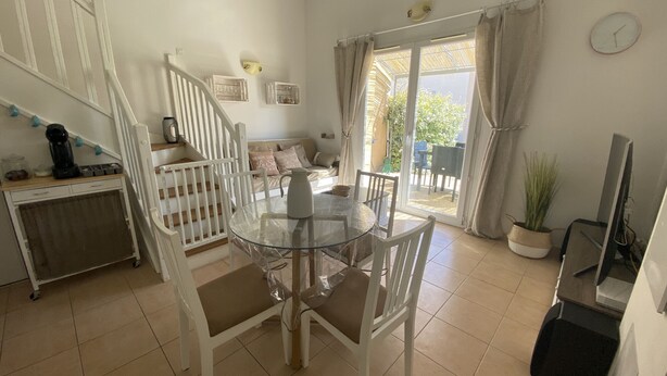 A dining area with a glass table and white chairs, a staircase with a white railing, a sofa with cushions, and a view of the outdoors through a glass door. - LS1-295 MARINADO Mouriès (Mouriès)