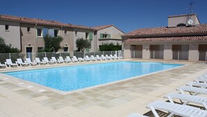 A swimming pool with white lounge chairs arranged around it, a tiled deck, and a building with a tiled roof in the background. - LS1-295 MARINADO Mouriès (Mouriès)