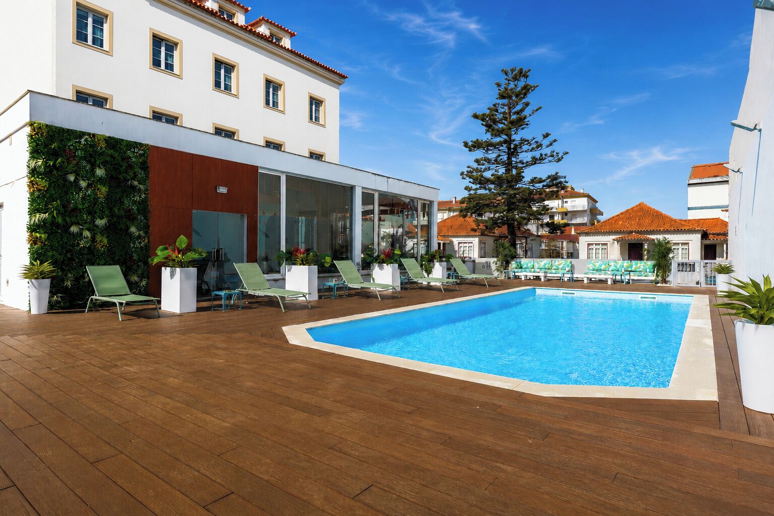 A swimming pool with lounge chairs, a wooden deck, and a building with a white facade and red-tiled roof.