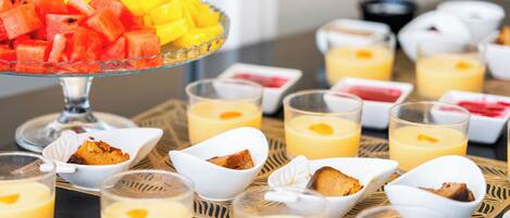 A breakfast buffet with various fruits, desserts, and beverages.