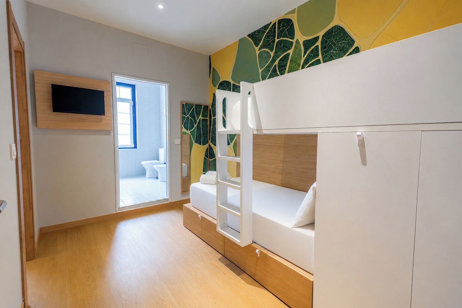 A room with a bunk bed, a TV mounted on the wall, and a bathroom visible through an open door.