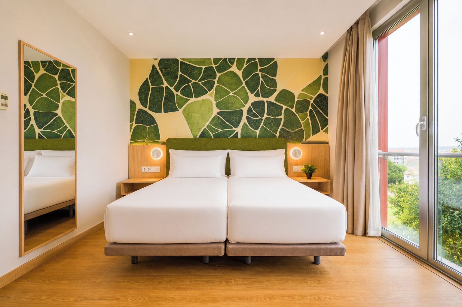 A double bed with a green leaf-patterned headboard, bedside tables with lamps, and a large window with a view of greenery.