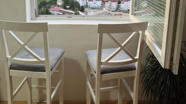 A room with two white chairs and a window overlooking a town and mountains.