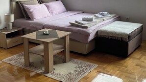 A bedroom with a bed, bedside table, lamp, and a window with blinds.