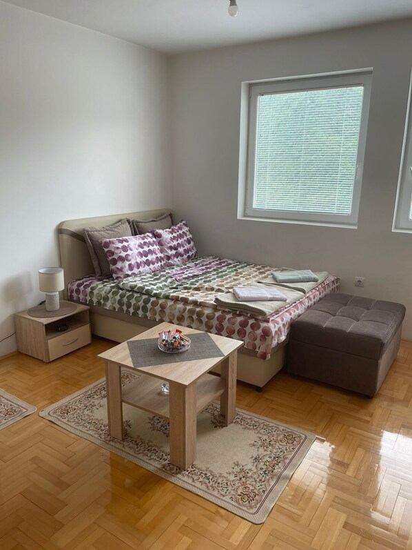 Ein Schlafzimmer mit Bett, Nachttischen, einem kleinen Tisch, einem Fenster und Blick ins Freie.