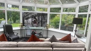 A conservatory with a sofa, a gaming chair, a desk with a computer, and a television. - Spacious 5-bed House - Garden, Parking & Bbq (Newcastle Upper)