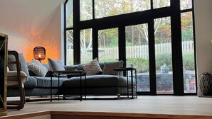 A modern living room with a large window, a sofa, and a staircase. - Spacious 5-bed House - Garden, Parking & Bbq (Newcastle Upper)