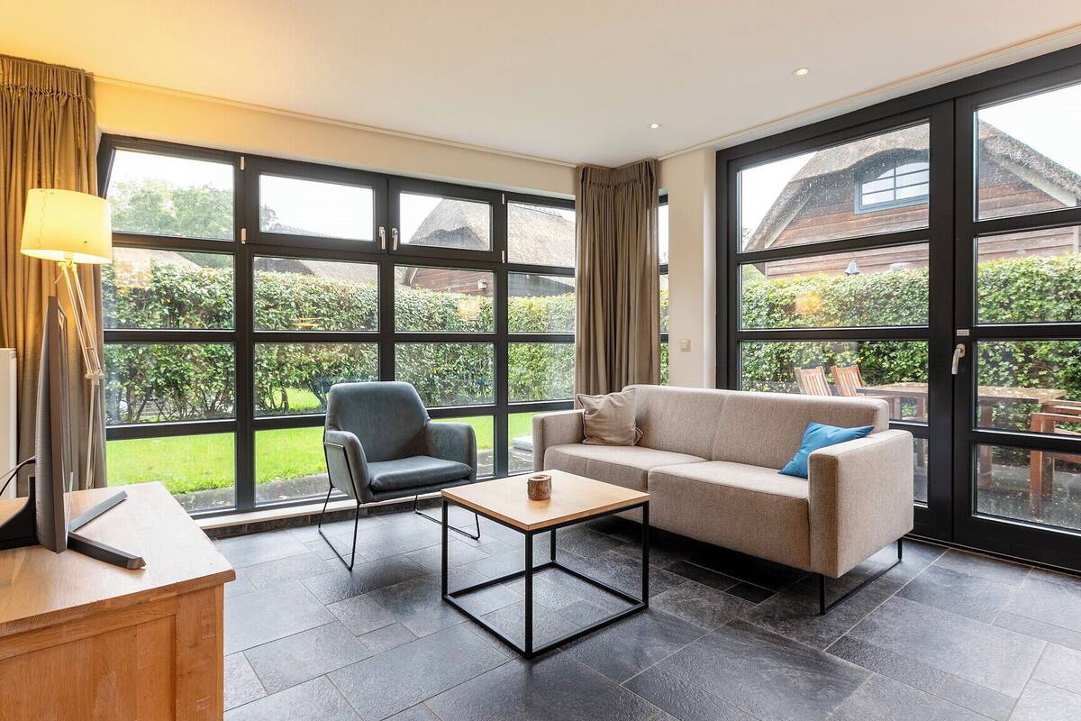 A modern living room with a sofa, armchair, and coffee table, large windows, and a view of the garden.