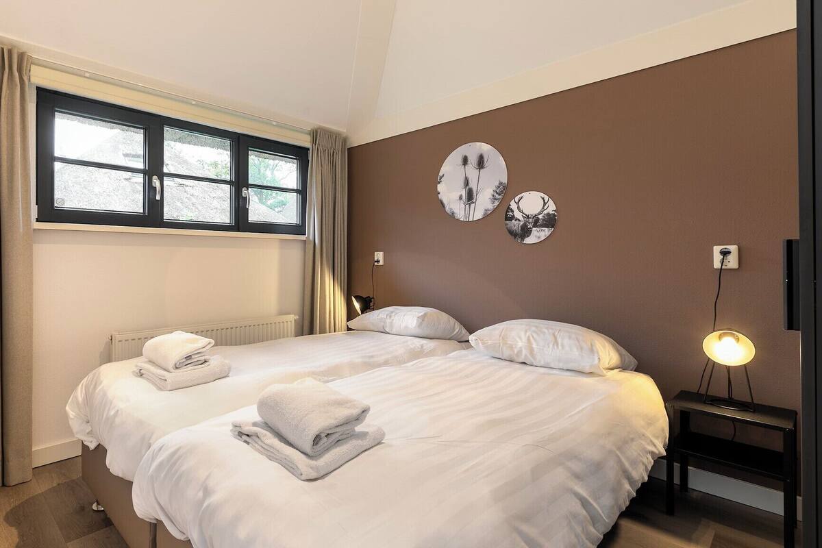 A hotel room with two beds, a window with curtains, a wall-mounted clock, and a bedside table with a lamp.