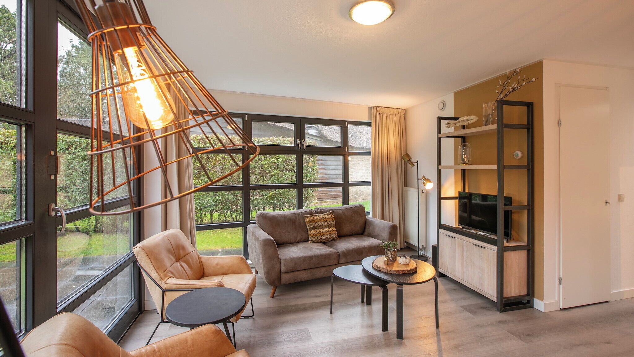 Una sala de estar moderna con sofá, sillón y una mesita de centro, ventanas amplias y un mueble empotrado para la televisión.