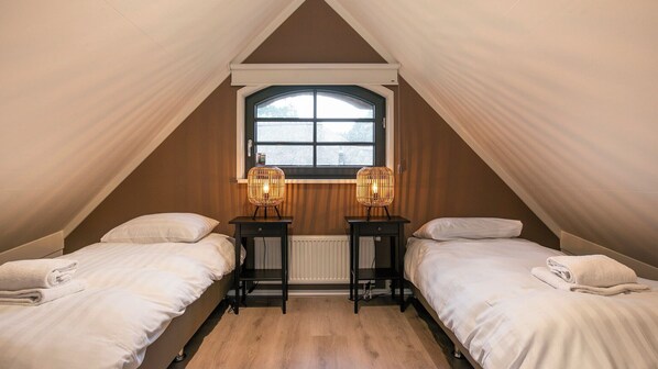 A cozy attic bedroom with two beds, a window, and two wall-mounted lamps.