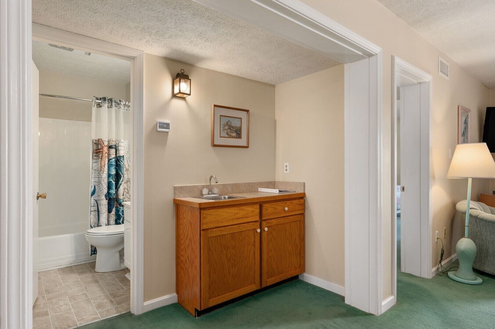 A bathroom with a wooden vanity, a toilet, a shower with a curtain, and a wall-mounted light fixture.