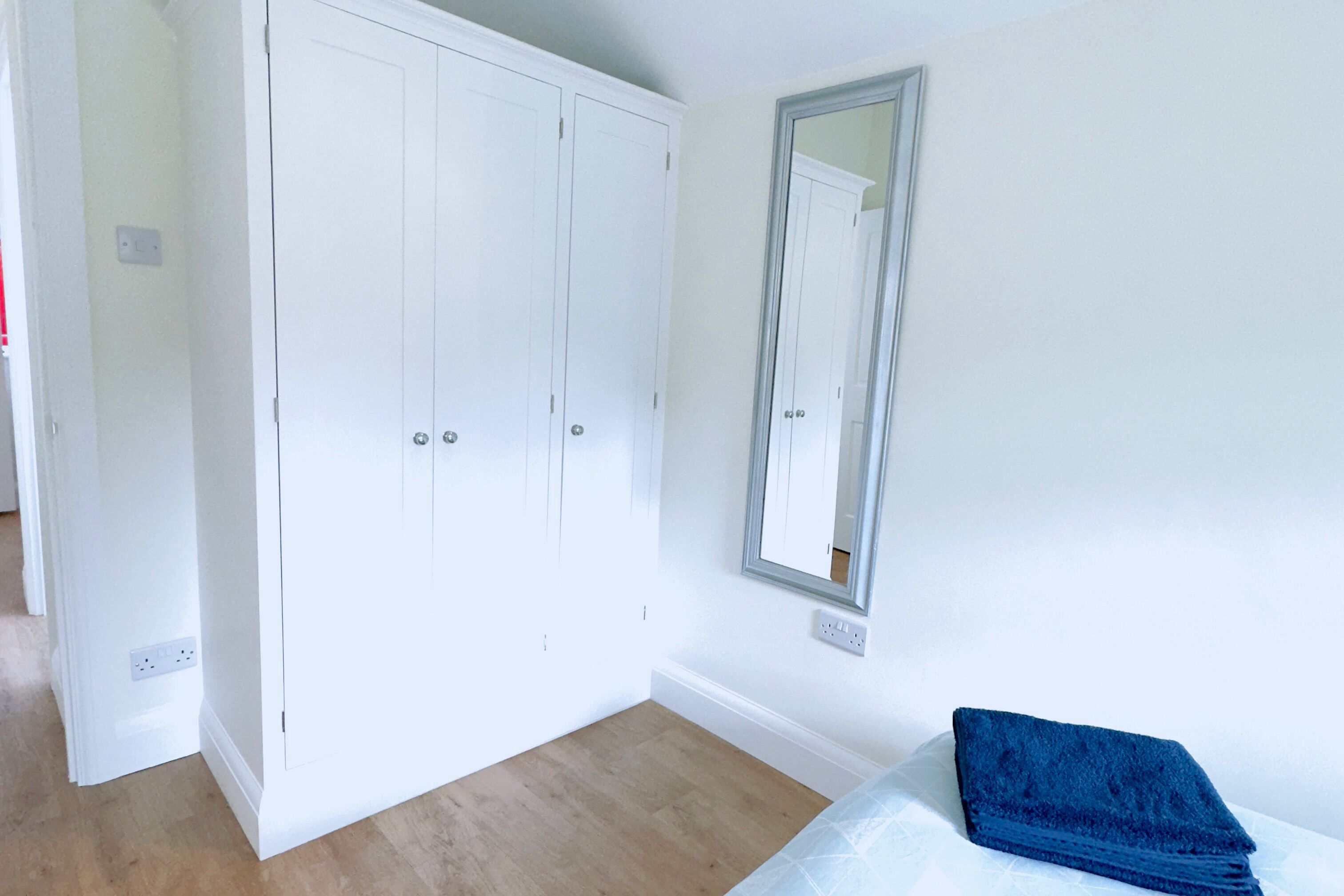 A bedroom with a white wardrobe, a mirror, and a blue towel on the bed.