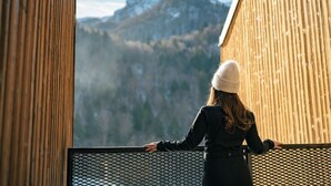 Une personne se tient sur un balcon, d’où l’on peut admirer un paysage de montagne.