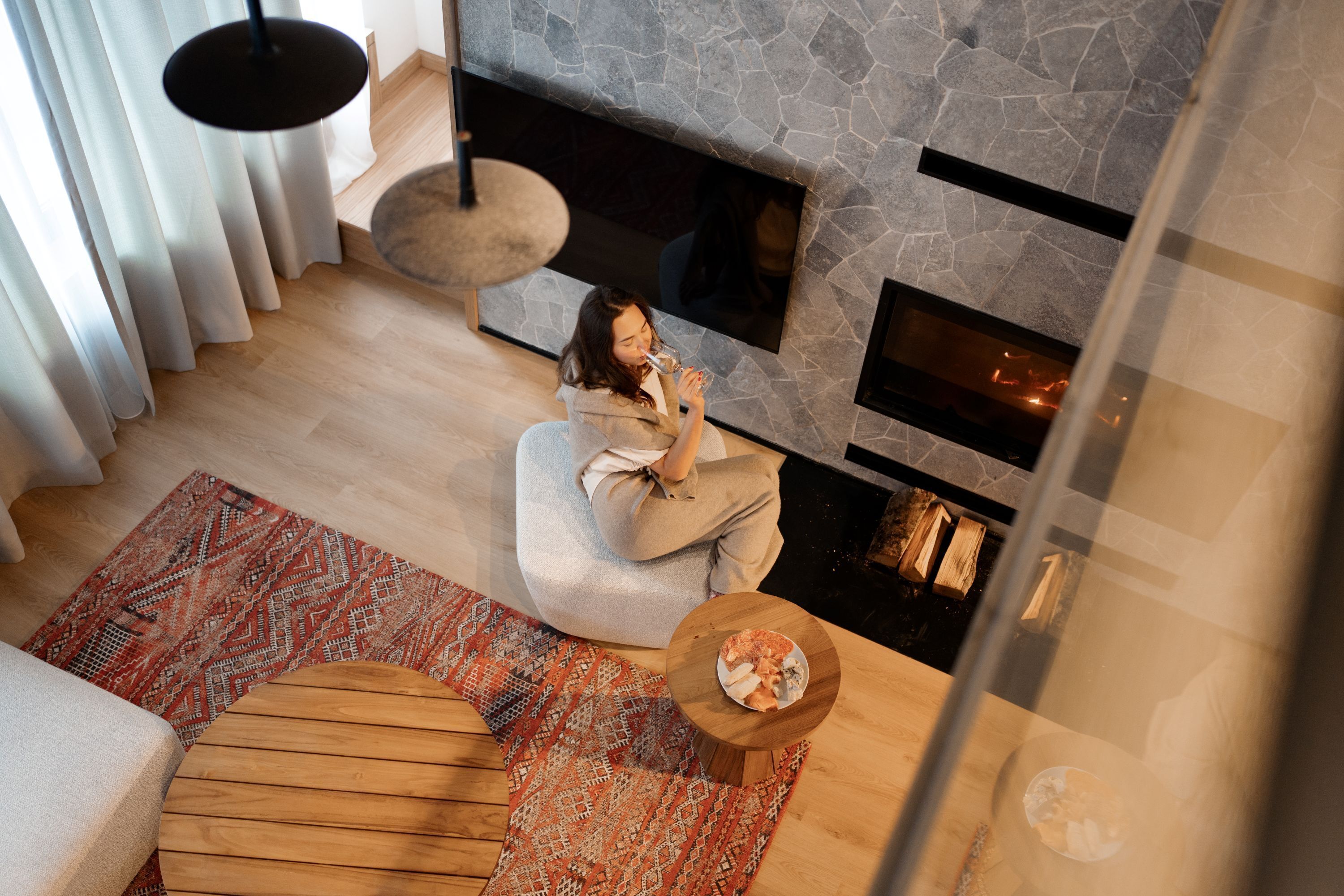 A modern living room with a stone fireplace, a wooden floor, and a patterned rug.