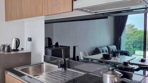 A modern kitchen with a stainless steel sink, a kettle, and a stove. There is a dining area with a table and chairs visible through a window. - NaiHarn Duplex with Pool View UTL A310 (Rawai)