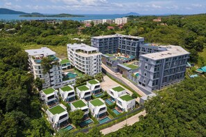 Un complesso residenziale moderno con diversi edifici, tetti verdi e una piscina centrale.