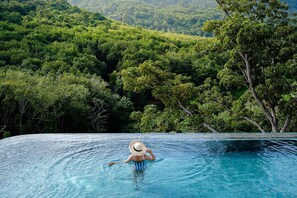 Una persona en una piscina con vistas a un bosque exuberante.
