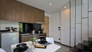 A modern kitchen with wooden cabinets, a built-in stove, and a dining area with a white table and black bowl. - NaiHarn Duplex with Pool View UTL A310 (Rawai)