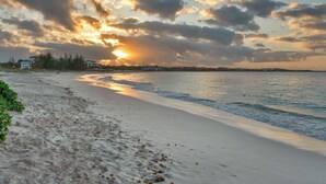 A beach with a sunset, sandy shore, and buildings in the background.