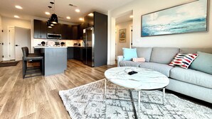 A modern living room with a grey sofa, a marble coffee table, and a kitchen in the background. - The LUX~ 1 Block to the Beach!! (Traverse City)