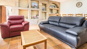 Un salon avec une cheminée en pierre, un fauteuil en cuir rouge, un canapé en cuir noir et une table basse en bois.