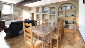 Un vaste espace dédié à la salle à manger, avec une table et des chaises en bois, un canapé noir, des murs en pierre et une cheminée en pierre.