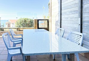 A patio with a granite table and white plastic chairs, a wooden wall, and a view of buildings and trees. - XILGAR Apartment Av Leon on the Beach (Sanxenxo)