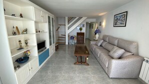 Un salon spacieux avec un canapé, une table basse et un téléviseur posé sur un meuble. Un escalier mène à un autre niveau.
