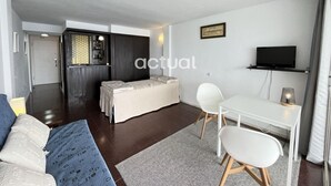 A modern living room with a sofa, a dining table with chairs, a TV, and a bar area with a counter and shelves.