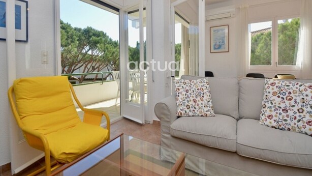 A living room with a yellow chair, a sofa with floral cushions, and a glass coffee table. - Apartment near beach with terrace and parking, optional aircon (Platja d'Aro)