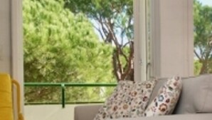 A room with a sofa, a yellow chair, and a view of trees through large windows. - Apartment near beach with terrace and parking, optional aircon (Platja d'Aro)