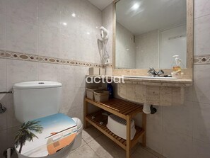 Et badeværelse med toilet, vask med spejl og en hylde med kurve.