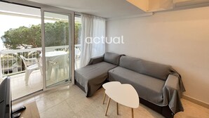 Una sala de estar moderna con un sofá gris, una mesita blanca y un ventanal corredero que da a un balcón exterior.