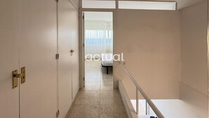 Un pasillo estrecho con una cama al final, una puerta a la izquierda y una ventana con cortinas al fondo.