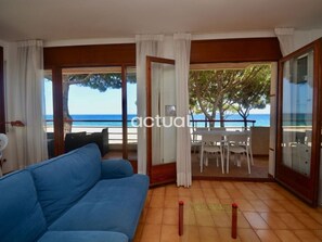 A room with a blue sofa, a dining table with chairs, and a view of the sea through large windows. - 4-bedroom seaside apartment in Platja d'Aro, optional parking (Platja d'Aro)