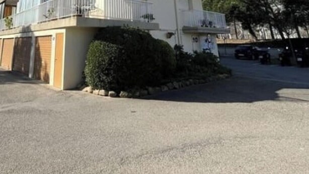 Un edificio residencial con entrada protegida por un portón, un pequeño jardín y un camino de acceso pavimentado.