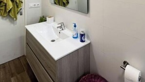 Un baño con lavamanos blanco, espejo y dispensador de papel higiénico.