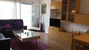 A living room with a sofa, coffee table, TV, wooden cabinets, and a glass door leading outside. - 3-bedroom apartment, pool & parking, 350 m from the beach (Platja d'Aro)