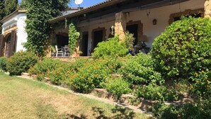 Un edificio tradicional con fachada de piedra, una antena parabólica y un jardín bien cuidado con diversas plantas y flores.