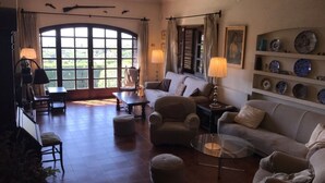 Amplia sala de estar con un ventanal grande, un sofá, sillones, una mesa de centro y una lámpara.