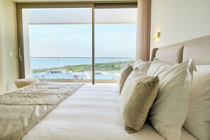 Quarto de hotel com uma grande porta de vidro deslizante que dá para uma varanda com vista para o mar e edifícios.