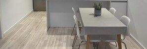 A modern dining area with a rectangular table, white chairs, and a potted plant.