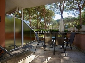 Una veranda coperta con tavolo e sedie, una porta scorrevole in vetro e vista su alberi e un edificio sullo sfondo.