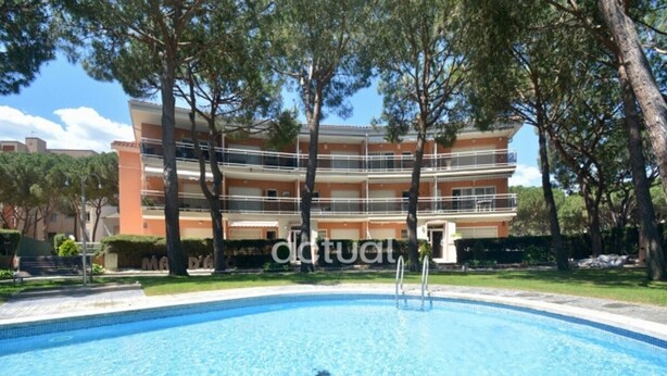 Une piscine à l’eau d’un bleu limpide, entourée d’une pelouse et d’arbres. Au fond, on aperçoit un immeuble à plusieurs étages doté de balcons.
