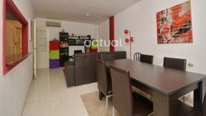 Un espace de salle à manger moderne, avec une grande table et des chaises, un luminaire suspendu rouge et une peinture abstraite aux couleurs vives accrochée au mur.